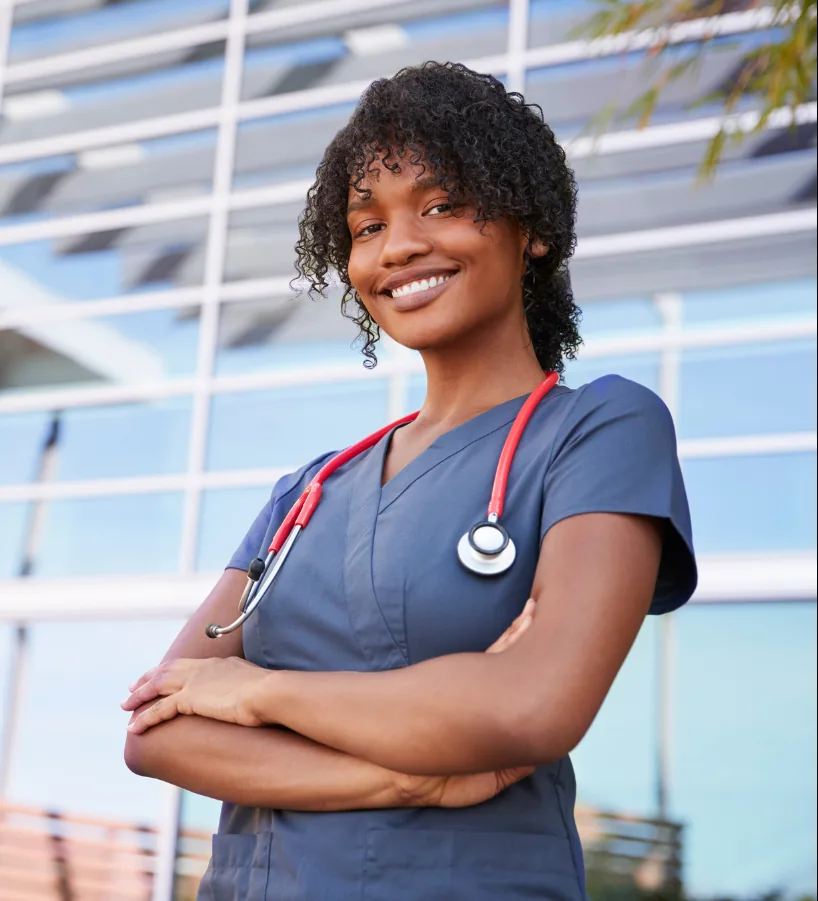 Smiling healthcare professional in scrubs with a stethoscope outside a medical office building